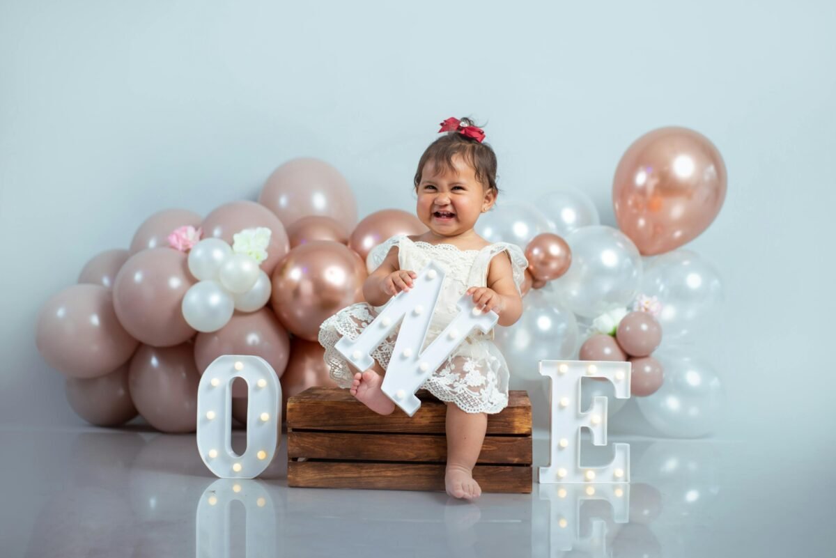 Cute baby girl celebrating her first birthday with balloons and decorations.