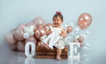 Cute baby girl celebrating her first birthday with balloons and decorations.